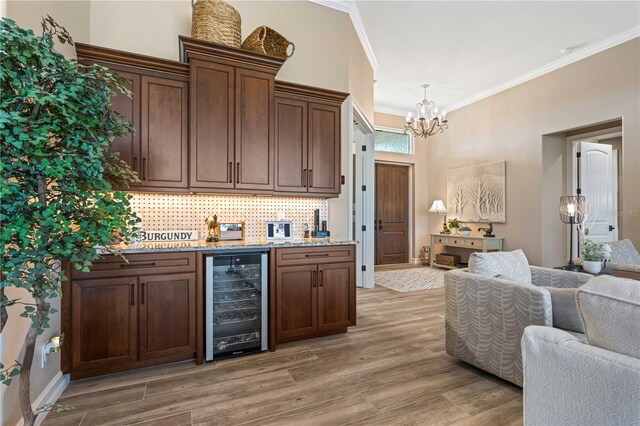 kitchen featuring light wood-style flooring, a chandelier, crown molding, wine cooler, and open floor plan
