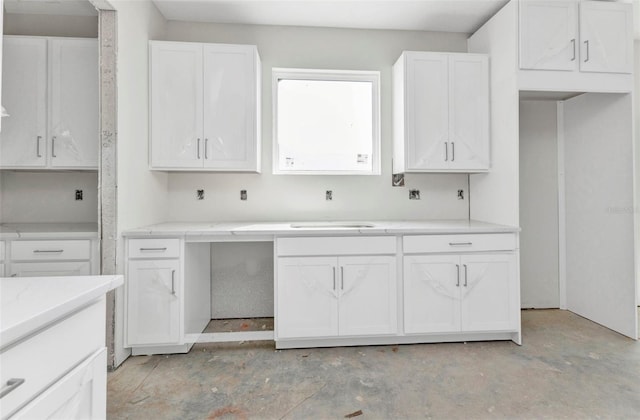 kitchen featuring light stone counters, concrete floors, white cabinetry, and a sink