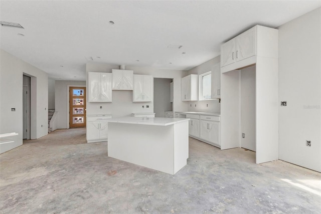 kitchen featuring unfinished concrete flooring, a center island, and white cabinetry