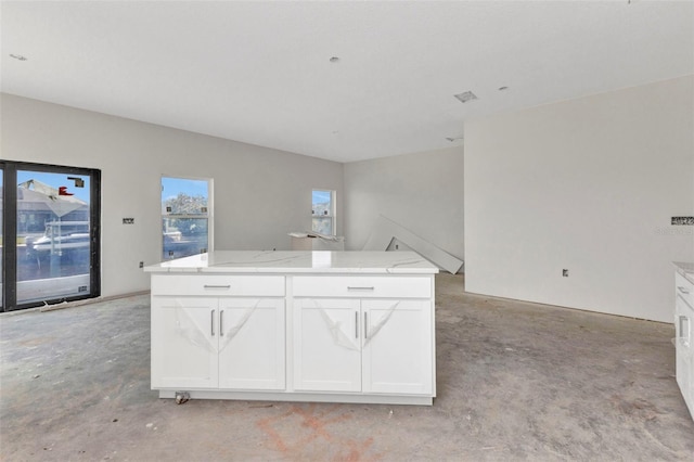 kitchen featuring a center island, open floor plan, white cabinetry, unfinished concrete flooring, and light stone counters