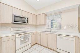 23482 Moreland Ave, Port Charlotte, FL 33954 - kitchen with light countertops, a sink, lofted ceiling, and white appliances