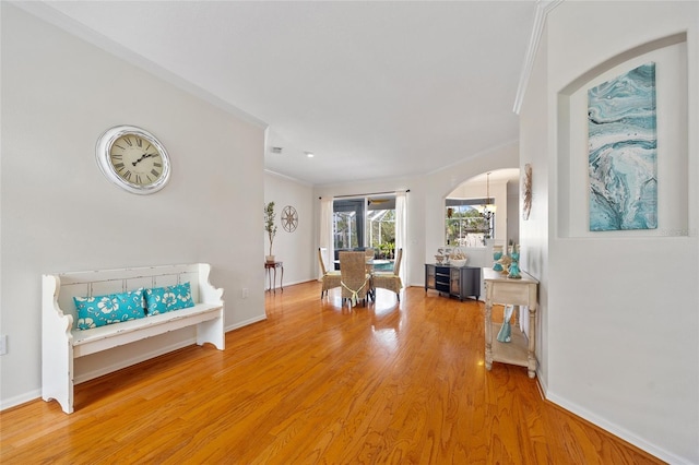 sitting room with crown molding, baseboards, light wood finished floors, and arched walkways