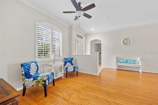living area featuring baseboards, crown molding, a ceiling fan, arched walkways, and wood finished floors