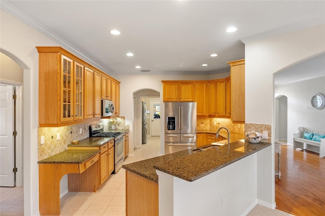 kitchen featuring a sink, appliances with stainless steel finishes, arched walkways, and dark stone counters