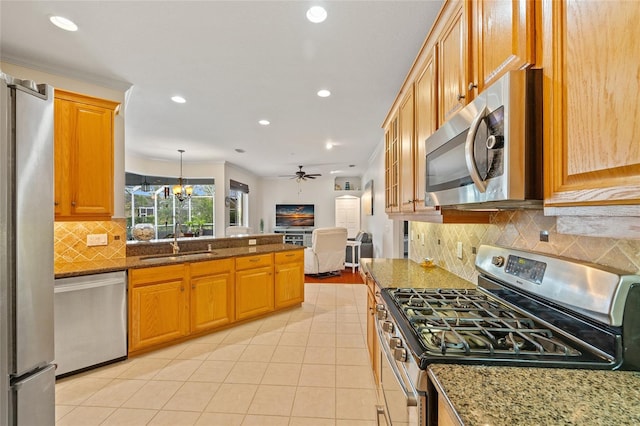 kitchen featuring stone counters, a peninsula, stainless steel appliances, ceiling fan with notable chandelier, and a sink