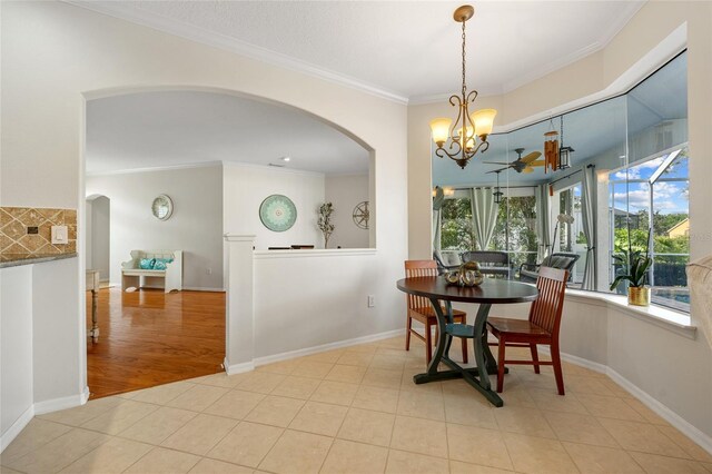 tiled dining area featuring crown molding, baseboards, arched walkways, and ceiling fan with notable chandelier