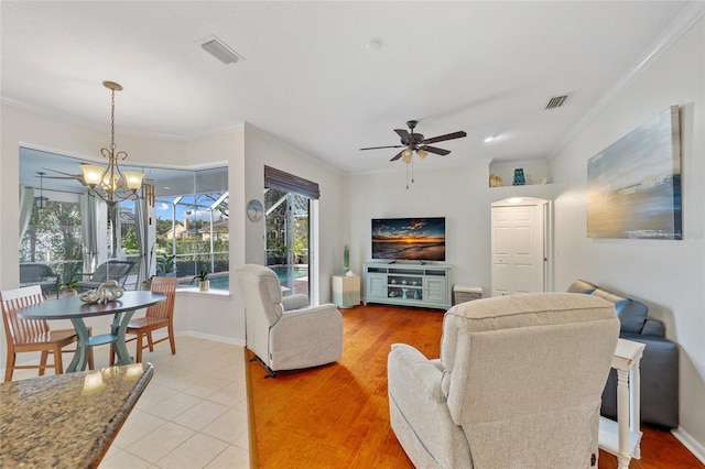 living area featuring baseboards, visible vents, ceiling fan with notable chandelier, and ornamental molding