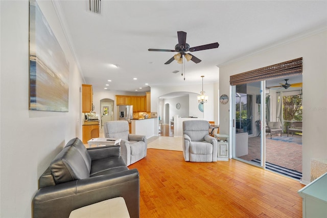 living area featuring arched walkways, ceiling fan with notable chandelier, and ornamental molding