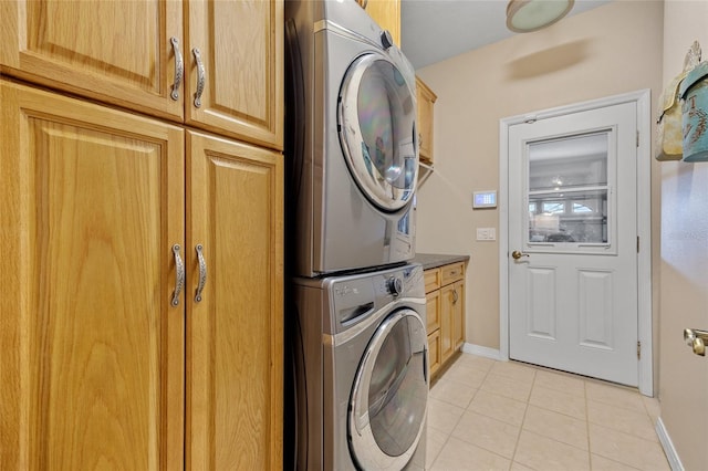 laundry room featuring stacked washer and dryer, light tile patterned floors, baseboards, and cabinet space