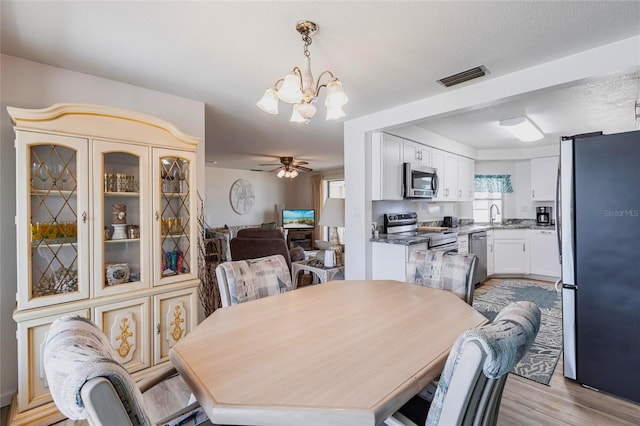 3249 Sunrise Trl, Port Charlotte, FL 33952 - dining space featuring a textured ceiling, visible vents, light wood-style floors, and ceiling fan with notable chandelier