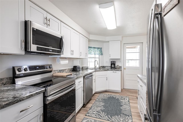 3249 Sunrise Trl, Port Charlotte, FL 33952 - kitchen with dark stone counters, a sink, light wood finished floors, white cabinets, and appliances with stainless steel finishes