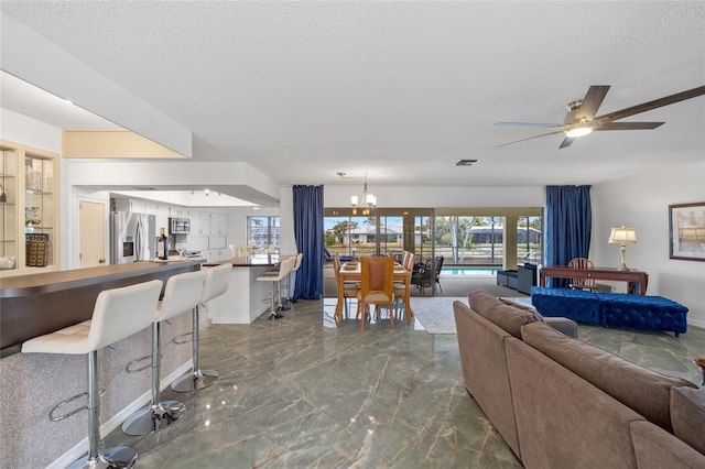 living area featuring marble finish floor, visible vents, ceiling fan with notable chandelier, and a textured ceiling
