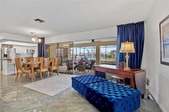 interior space featuring a textured ceiling, baseboards, marble finish floor, ceiling fan with notable chandelier, and visible vents