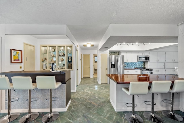 kitchen featuring a kitchen bar, a peninsula, stainless steel appliances, marble finish floor, and dark countertops