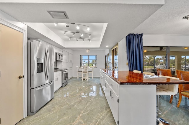 kitchen with a textured ceiling, visible vents, marble finish floor, stainless steel appliances, and a raised ceiling