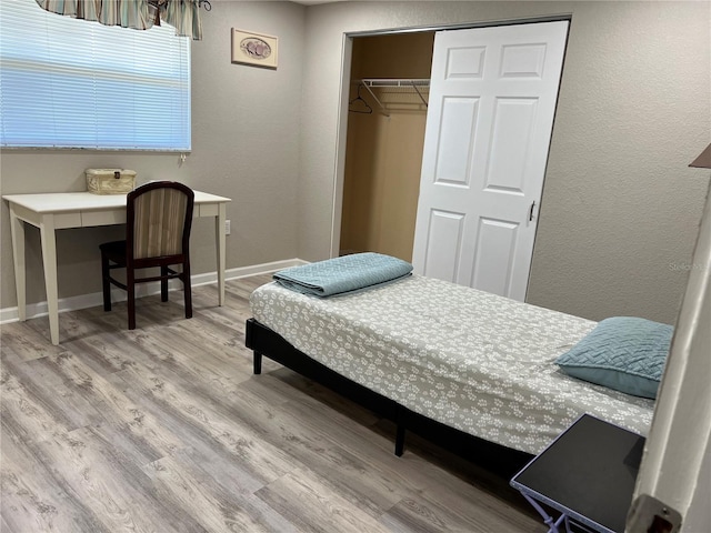 bedroom featuring a textured wall, baseboards, a closet, and wood finished floors