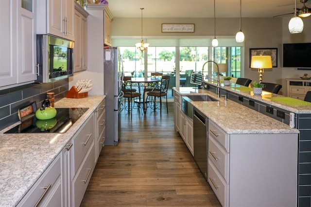 kitchen featuring tasteful backsplash, a sink, a kitchen island with sink, stainless steel appliances, and dark wood-style floors