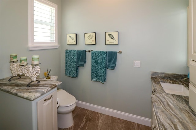 half bath with baseboards, vanity, and toilet