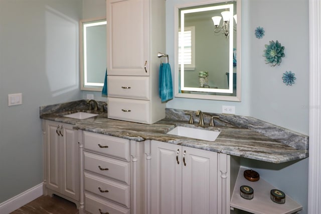 full bath with an inviting chandelier, double vanity, baseboards, and a sink