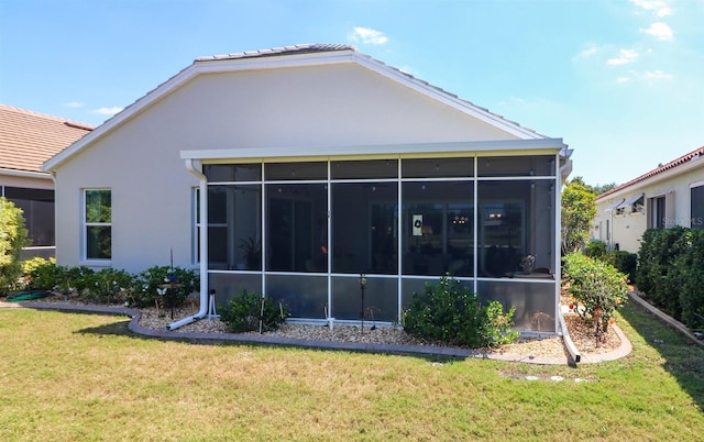 back of house featuring a sunroom, a tiled roof, stucco siding, and a lawn