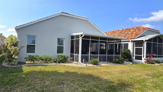 rear view of property with a sunroom, a yard, and stucco siding