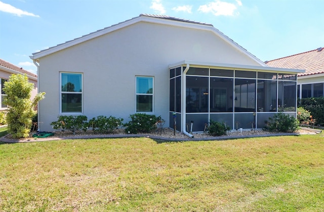 rear view of house featuring a sunroom, stucco siding, and a lawn