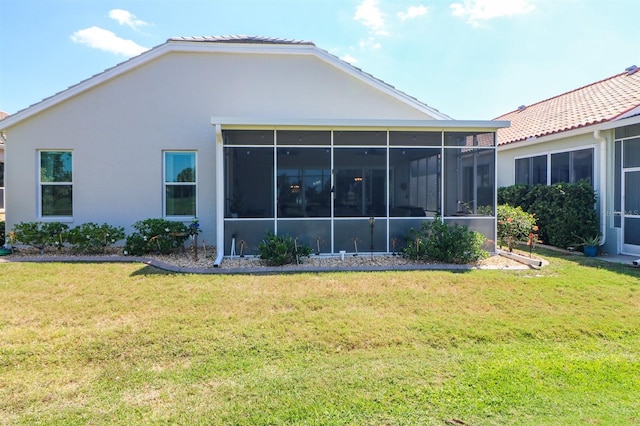 back of house with a lawn, a sunroom, and stucco siding
