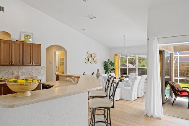 kitchen featuring arched walkways, a sink, light countertops, light wood-type flooring, and a kitchen bar