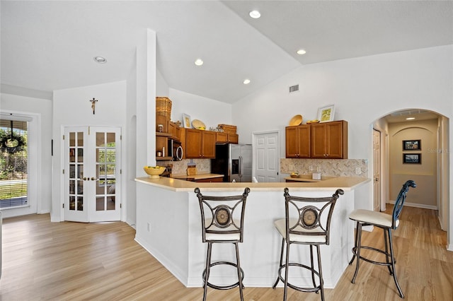 kitchen with brown cabinets, arched walkways, lofted ceiling, and stainless steel appliances