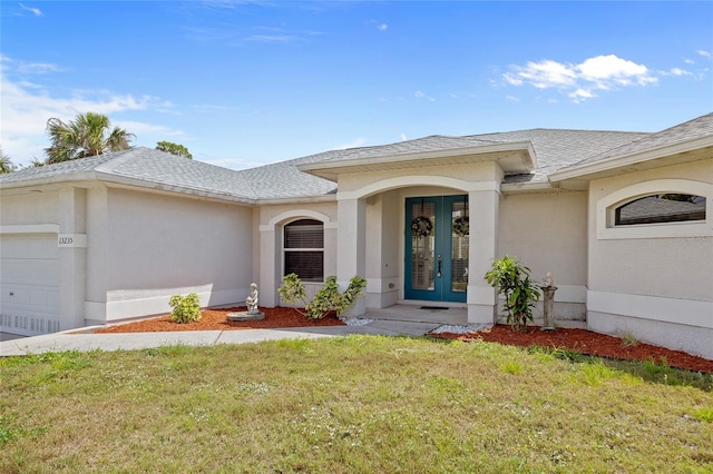 doorway to property with a shingled roof, a yard, a garage, stucco siding, and french doors