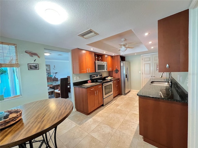 931 Juno Dr, Punta Gorda, FL 33950 - kitchen with stainless steel appliances, a raised ceiling, brown cabinetry, dark stone countertops, and a ceiling fan