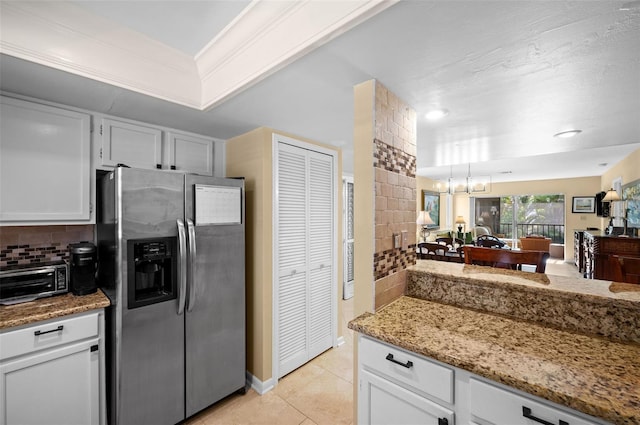 kitchen with stainless steel fridge, an inviting chandelier, light tile patterned floors, decorative backsplash, and light stone counters