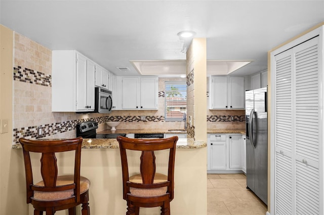 kitchen featuring tasteful backsplash, a peninsula, light tile patterned floors, stainless steel appliances, and white cabinets