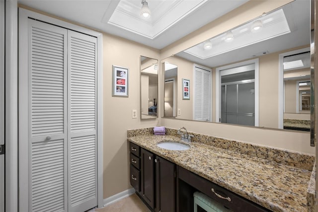 full bathroom with vanity, a tray ceiling, baseboards, a shower stall, and a closet