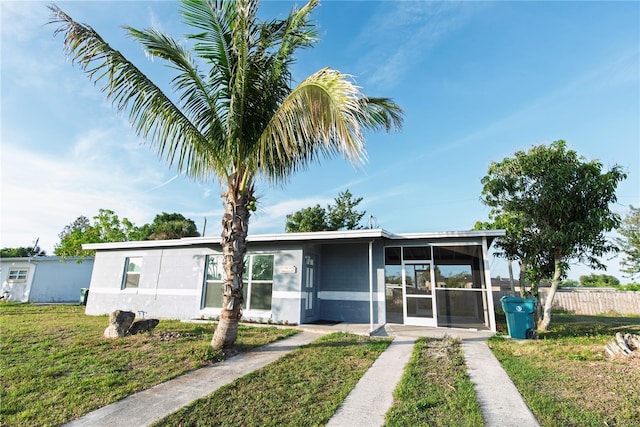view of front facade with a front yard, a sunroom, stucco siding, and fence