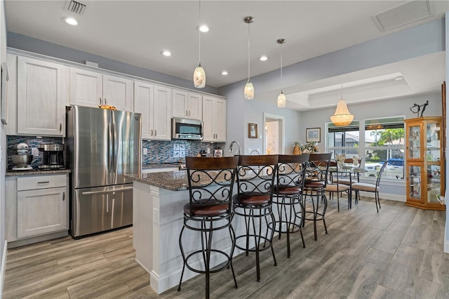 kitchen featuring a kitchen island with sink, stainless steel appliances, a tray ceiling, and visible vents