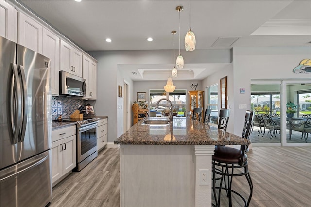 kitchen with a sink, backsplash, appliances with stainless steel finishes, a center island with sink, and light wood-style floors