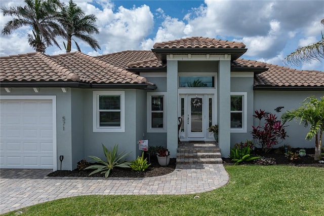 mediterranean / spanish house with a tiled roof, driveway, stucco siding, and an attached garage