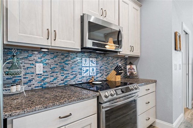 kitchen with white cabinets, baseboards, dark stone counters, stainless steel appliances, and backsplash