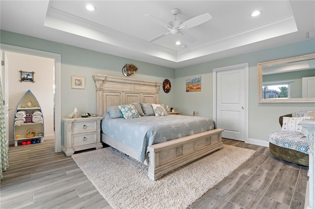 bedroom with a tray ceiling, light wood finished floors, ornamental molding, and recessed lighting