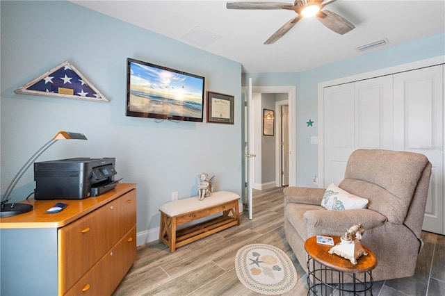 living area featuring baseboards, light wood-style flooring, visible vents, and a ceiling fan