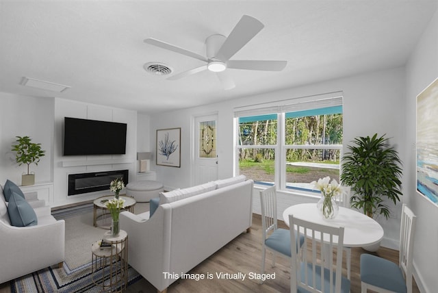 living area with a glass covered fireplace, a ceiling fan, baseboards, wood finished floors, and visible vents