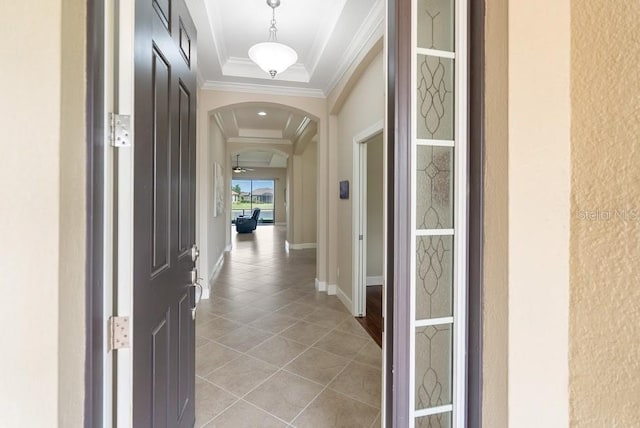 hallway with baseboards, ornamental molding, light tile patterned floors, a tray ceiling, and arched walkways