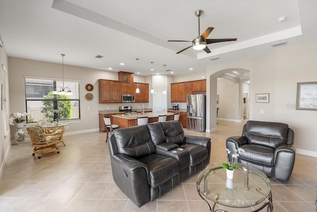 living area featuring ceiling fan, arched walkways, visible vents, a raised ceiling, and baseboards