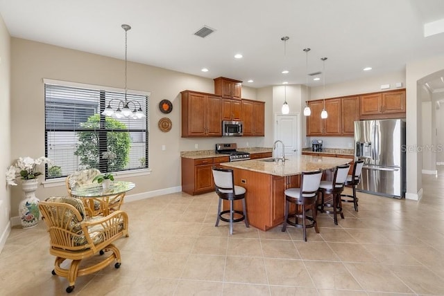 kitchen with brown cabinetry, visible vents, appliances with stainless steel finishes, light stone counters, and a sink