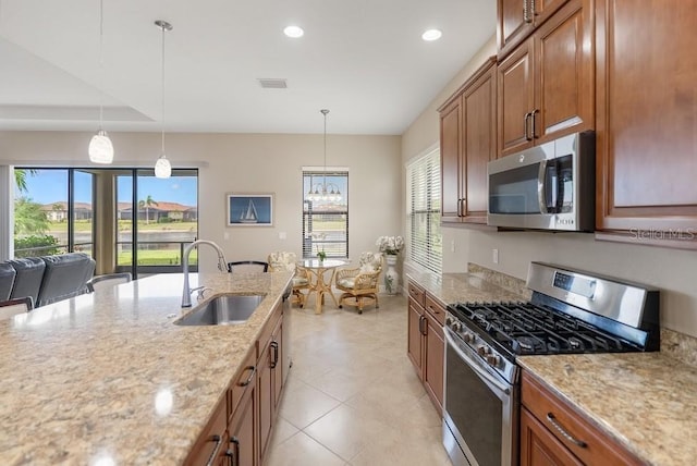 kitchen with light stone counters, brown cabinets, appliances with stainless steel finishes, pendant lighting, and a sink