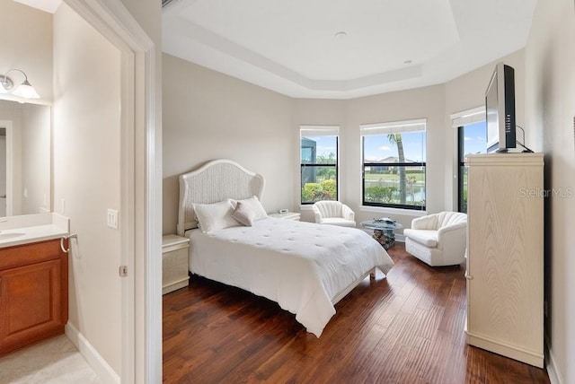 bedroom with a raised ceiling, wood finished floors, and baseboards
