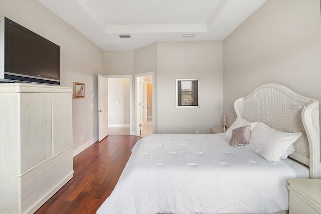 bedroom with visible vents, baseboards, wood finished floors, and a raised ceiling