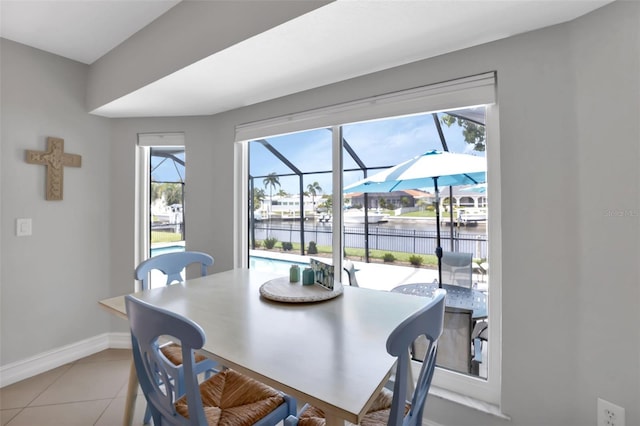 dining space featuring a sunroom, tile patterned floors, baseboards, and a water view