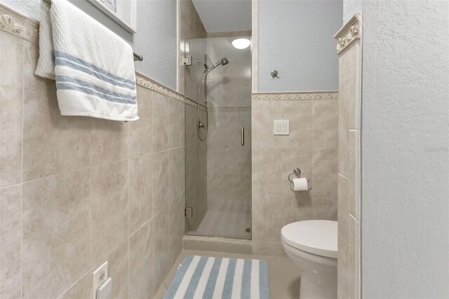 full bath with toilet, tile walls, and a stall shower